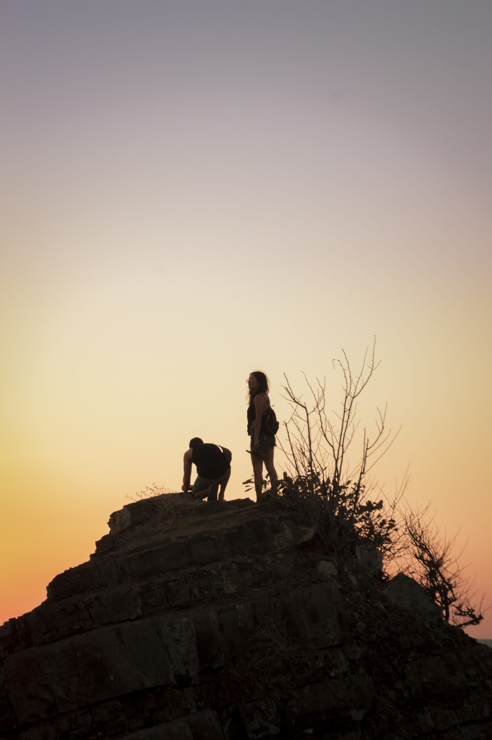 boy and girl on a rock watching the sunset, silhouettes of coupl