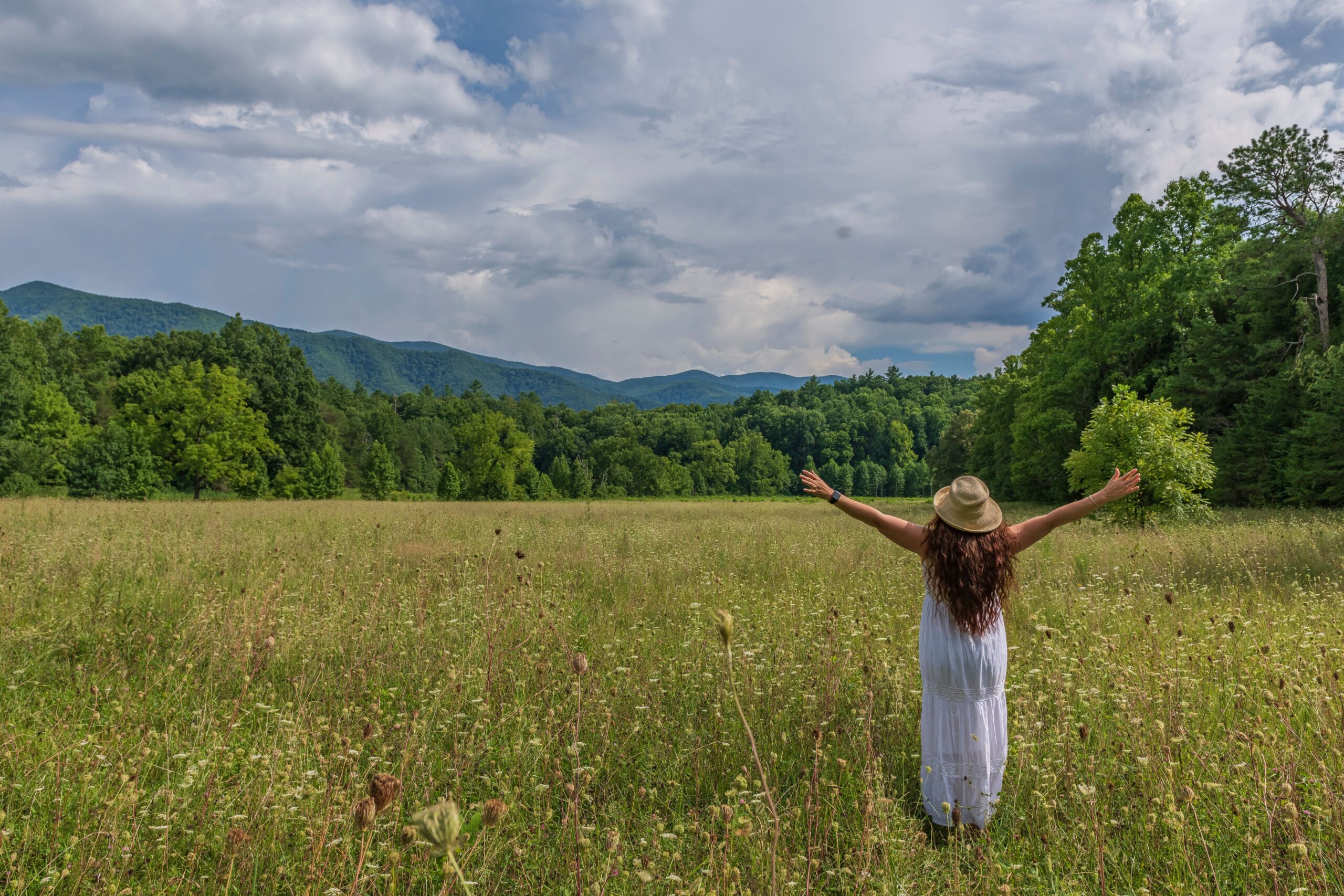 female with open arms standing middle field with vegetation background (1)